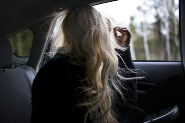 Teenager mit langen Haaren schaut durch ein Fenster im Auto - CAVF23938