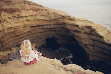 Rear view of woman sitting on rock formation by sea - CAVF23954