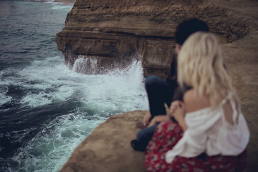 Romantic couple sitting on rock formation by sea - CAVF23955