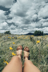 Low section of woman on grass against cloudy sky - CAVF23956