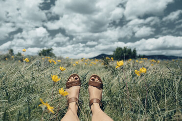 Niedriger Ausschnitt einer Frau auf einem grasbewachsenen Feld vor einer Wolkenlandschaft - CAVF23958