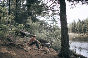 Side view of man with Australian Shepherd by lake in forest - CAVF23966