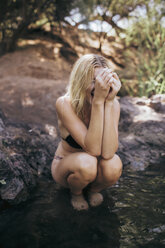 Happy woman in bikini crouching at lakeshore - CAVF23980