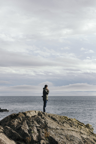 Seitenansicht eines Mannes, der auf einer Felsformation am Meer steht, gegen einen bewölkten Himmel, lizenzfreies Stockfoto