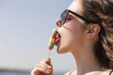 Seitenansicht der verführerischen Frau leckt Eis Lolly gegen klaren Himmel - CAVF24037