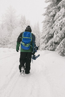 Rückansicht eines Mannes mit Snowboard auf einem schneebedeckten Feld - CAVF24042