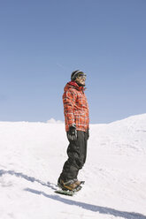Man looking away while standing on snowboard at field during winter - CAVF24045