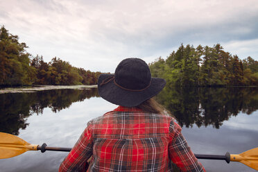 Rear view of woman kayaking in lake at forest against sky - CAVF24066