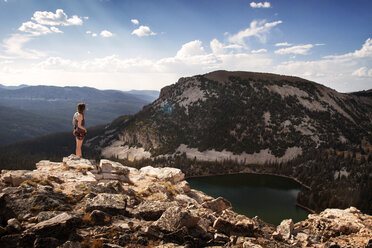 Woman standing on cliff by lake against sky - CAVF24076