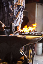 Beschnittenes Bild eines Handwerkers, der in einer Fabrik Metall aufhämmert - CAVF24130