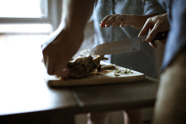 Midsection of friends cutting cooked lamb at table - CAVF24182