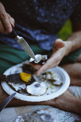 Low section of man shucking oyster shell while sitting on blanket at lawn - CAVF24190