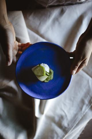 Draufsicht auf eine Frau, die eine Gurke und einen Reiswickel in einem Teller am Esstisch hält, lizenzfreies Stockfoto