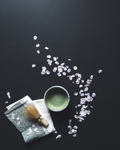 Overhead-Ansicht von Matcha-Tee und Bambus Schneebesen von Blütenblättern auf schwarzem Hintergrund, lizenzfreies Stockfoto