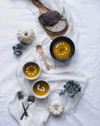 Draufsicht auf eine in Schalen servierte Suppe mit Kürbissen und Broten auf Textil - CAVF24312