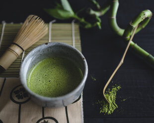 Overhead view of matcha tea in bowl with spoon and whisk on table - CAVF24318