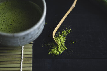 Close-up of matcha tea in bowl with ground and bamboo spoon on table - CAVF24319