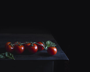 Frische rote Tomaten auf einem Tisch vor einer schwarzen Wand - CAVF24326