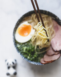 High angle view of noodles in chopsticks over bowl of soup and pork - CAVF24354