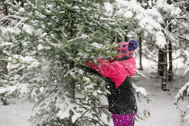 Side view of girl playing with snow covered tree - CAVF24391