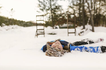 Porträt eines Mädchens, das mit den Augen zwinkert, während es auf einem schneebedeckten Feld liegt - CAVF24400