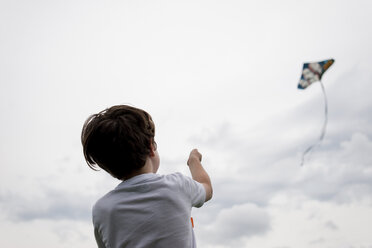 Rear view of boy flying kite in cloudy sky - CAVF24425