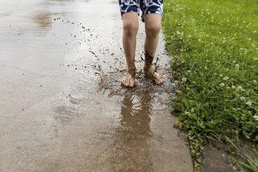 Low section of boy jumping in dirty puddle - CAVF24442