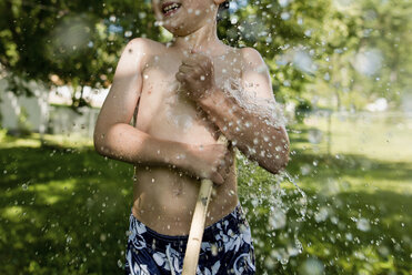 Mittelteil eines glücklichen Jungen ohne Hemd, der mit Wasser im Hinterhof spielt - CAVF24444