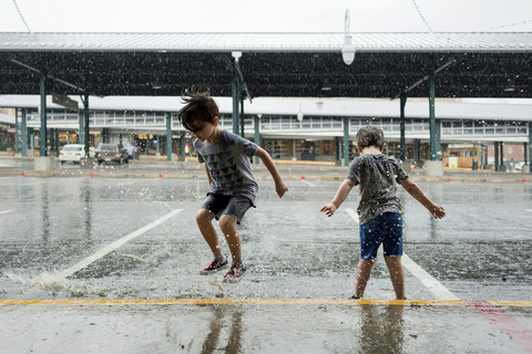 Glückliche Brüder spielen auf einem Parkplatz im Monsun, lizenzfreies Stockfoto
