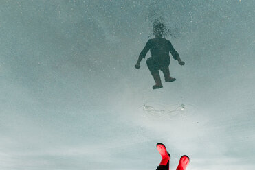 Niedriger Ausschnitt eines Jungen, der sich auf dem Wasser spiegelt, während er auf der Straße in eine Pfütze springt - CAVF24465