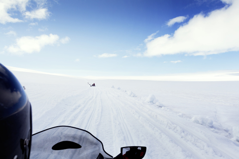 Abgeschnittenes Bild einer Person, die mit einem Schneemobil durch die Landschaft fährt, gegen den Himmel, lizenzfreies Stockfoto