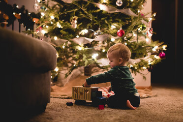 Seitenansicht der niedlichen Baby-Junge spielt mit Spielzeug-LKW von Weihnachtsbaum zu Hause - CAVF24554