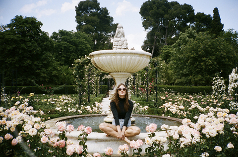 Porträt einer Frau, die auf einem von Rosen umgebenen Springbrunnen im Park sitzt, lizenzfreies Stockfoto