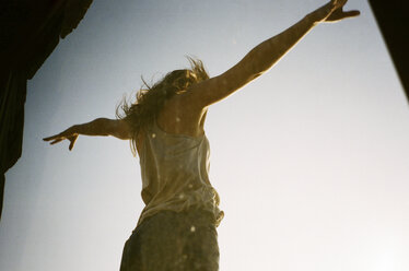 Low angle view of woman standing with arms outstretched against clear sky seen through glass - CAVF24597