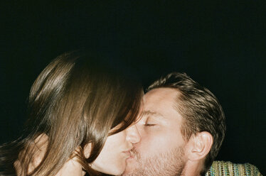 Nahaufnahme eines zärtlichen Paares, das sich vor einem schwarzen Hintergrund küsst - CAVF24615