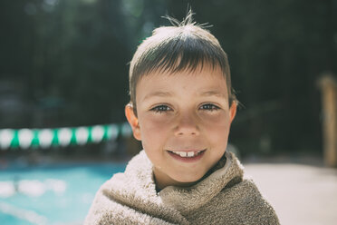 Portrait of happy boy wrapped in a towel standing at poolside - CAVF24654