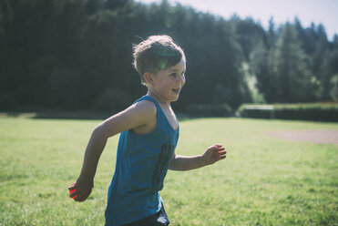 Seitenansicht eines glücklichen Jungen, der mit einem Ball im Park läuft - CAVF24665