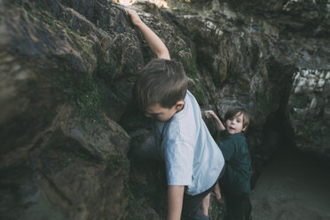 Brothers climbing on rock formations at beach - CAVF24669