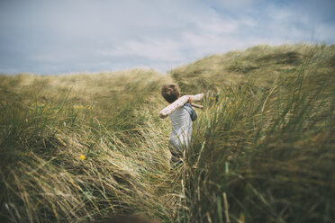 Rear view of boy carrying firewood on shoulders while walking amidst grassy field at A_o Nuevo State Park - CAVF24683