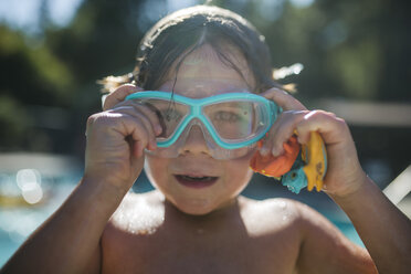 Porträt eines Jungen ohne Hemd, der seine Schwimmbrille am Pool einstellt - CAVF24690