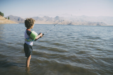 Side view of boy fishing while standing in river during sunny day