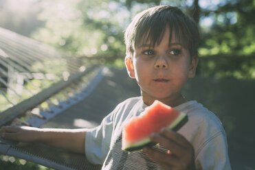 Boy eating watermelon against hammock during sunny day - CAVF24713