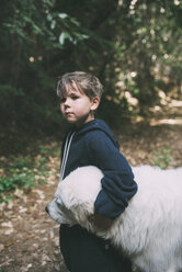 Thoughtful boy embracing dog while standing at park - CAVF24715