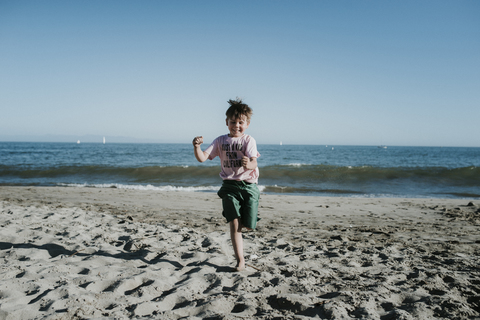 Carefree boy running at beach against clear sky during sunny day stock photo