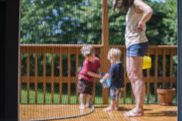 Tiefschnitt einer Mutter mit Kindern in der Veranda durch eine Glastür gesehen - CAVF24733