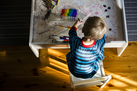 Hoher Blickwinkel auf einen Jungen, der auf einem Tisch sitzt und zeichnet, lizenzfreies Stockfoto