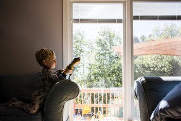 Junge spielt mit Spielzeug, während er zu Hause auf einem Sessel kniet - CAVF24755