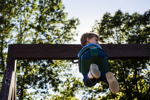 Niedriger Blickwinkel des Jungen schaukeln gegen den Himmel auf dem Spielplatz, lizenzfreies Stockfoto