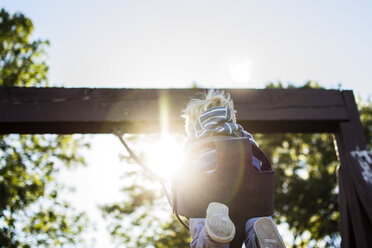 Low angle view of boy swinging in playground on sunny day - CAVF24765