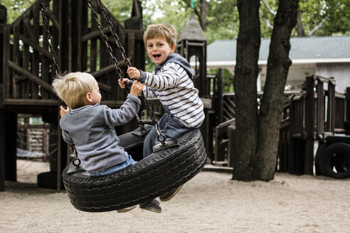 Glückliche Brüder, die sich auf einer Reifenschaukel auf dem Spielplatz vergnügen - CAVF24767